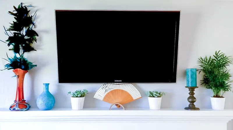 wall mounted TV over fireplace with decor hiding the outlet