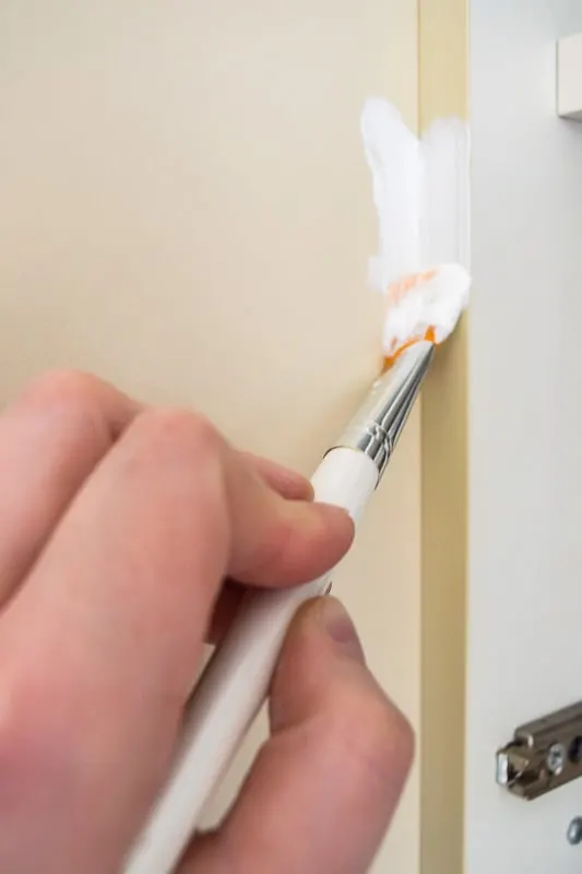 using paint brush to paint trim on melamine cabinets