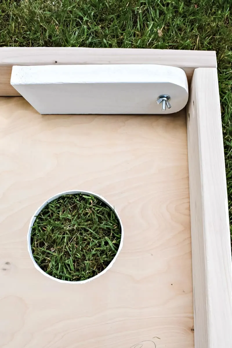 collapsible leg of DIY cornhole board inside frame with circular hole