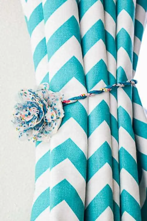 turquoise and white chevron curtain held open with a magnetic curtain tie back with a faux flower decoration