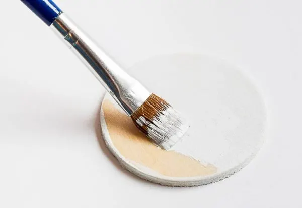 wooden circle being painted white with small paintbrush