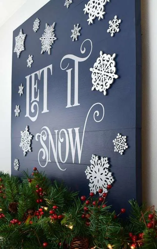 side view of wood Let it Snow sign on mantle with Christmas garland in front