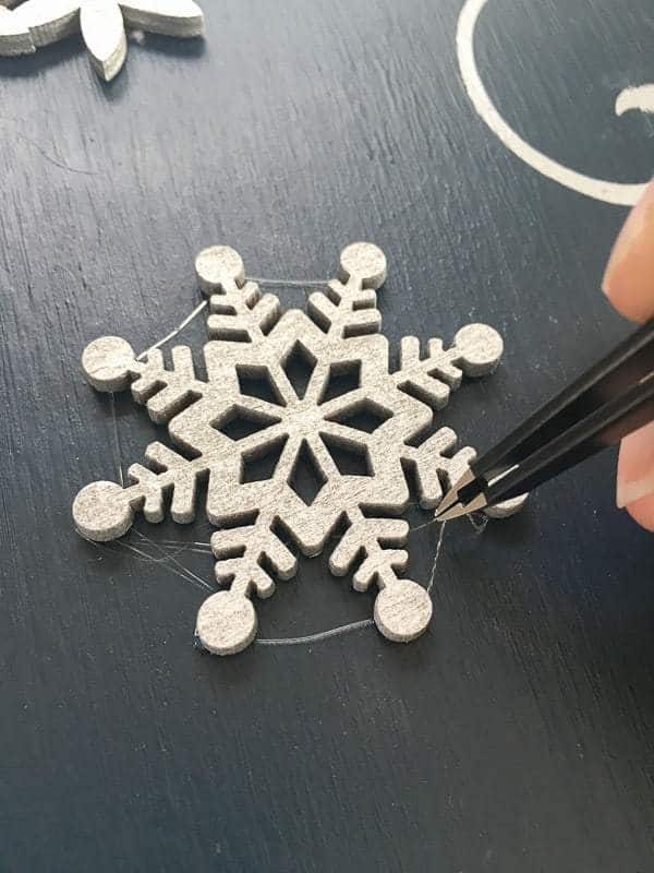 removing excess glue from wooden snowflakes on Let it Snow sign with tweezers