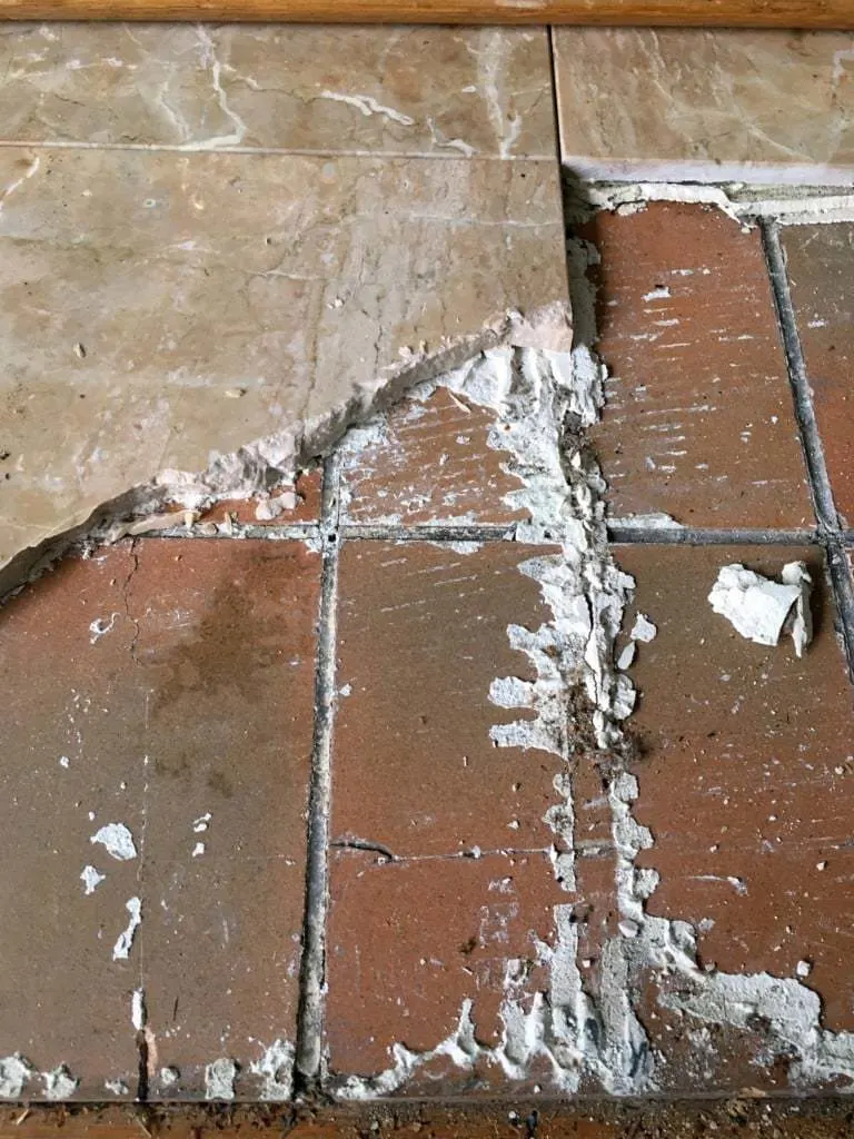 fireplace hearth with top layer of tile partially removed to reveal more tile underneath