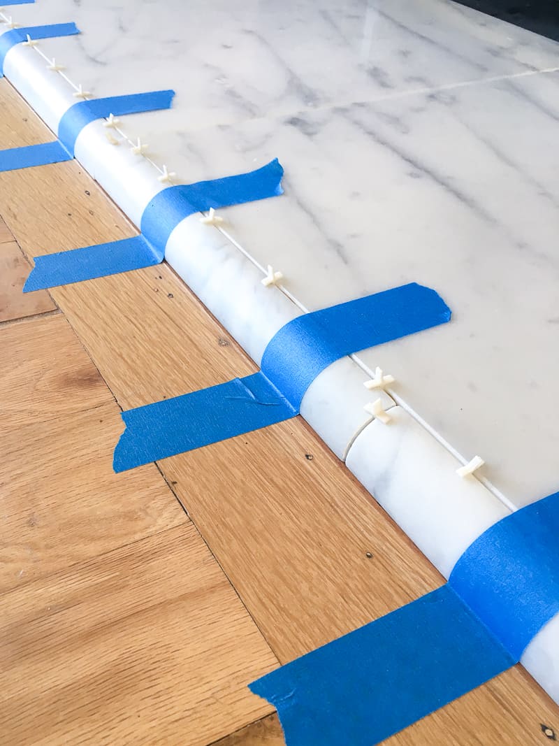 painter's tape used to hold quarter round tile to edge of fireplace hearth