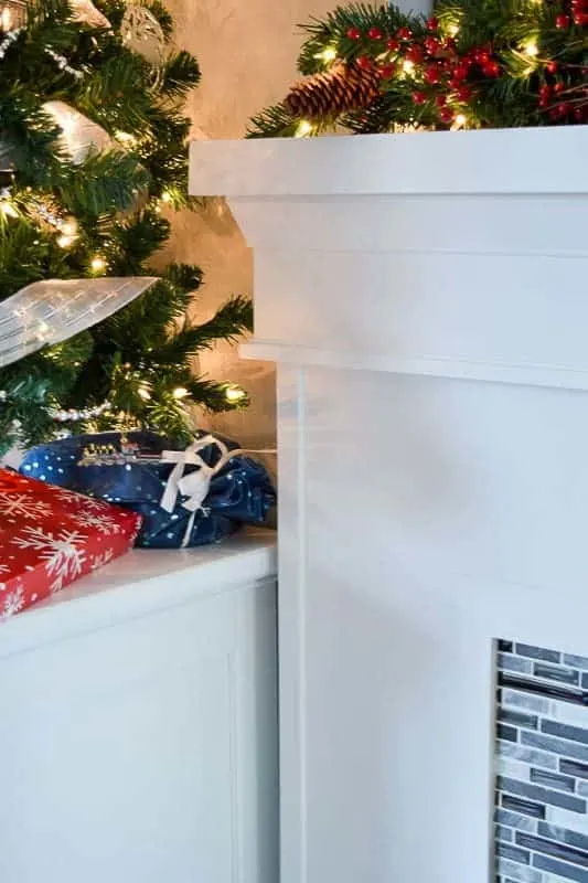 storage cabinet next to fireplace with small Christmas tree and wrapped gifts on top