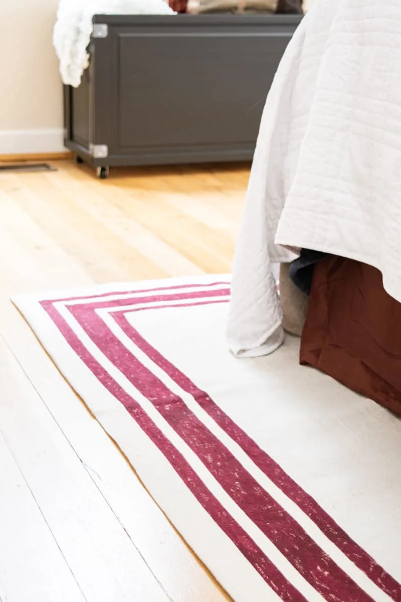 DIY rug with red stripes under bed with red bed skirt and blanket box in the background