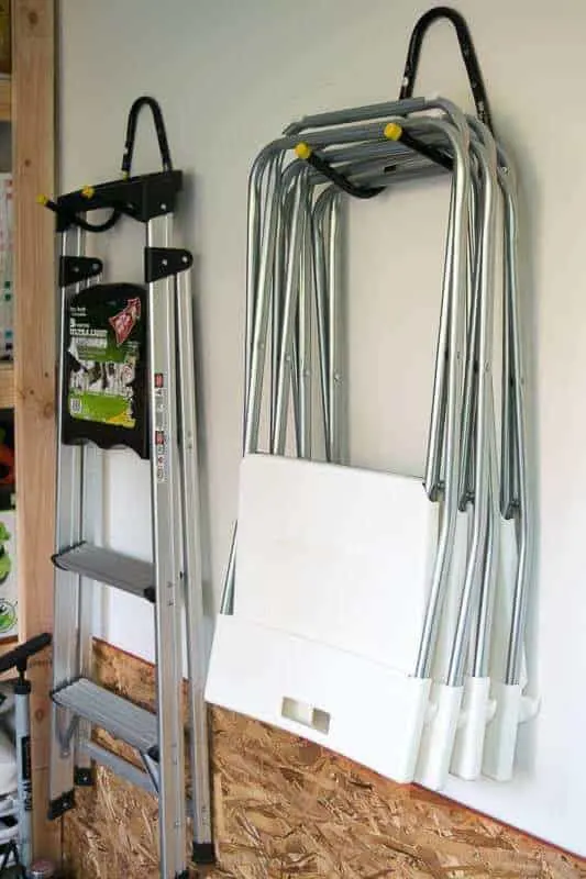 ladder and folding chairs hung on the wall next to shed shelving