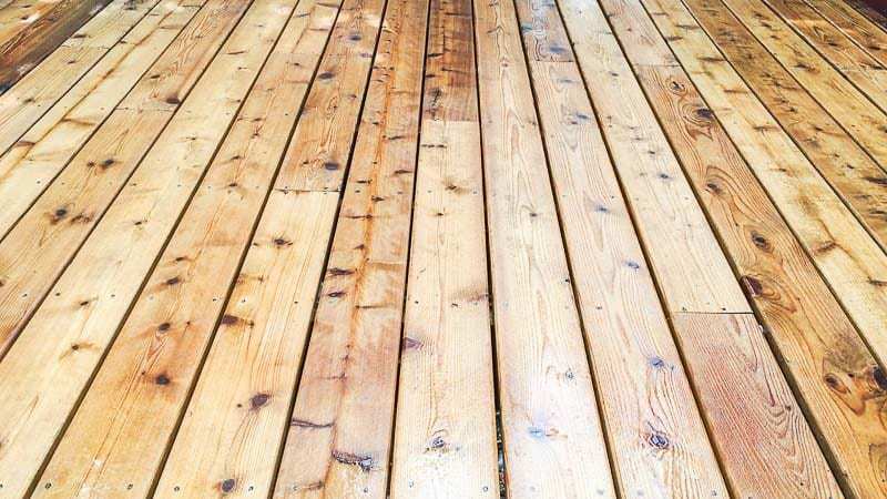 spraying wood brightener on wooden deck