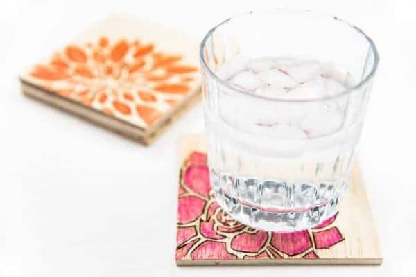 DIY wood burned coasters with painted floral designs under glass of water