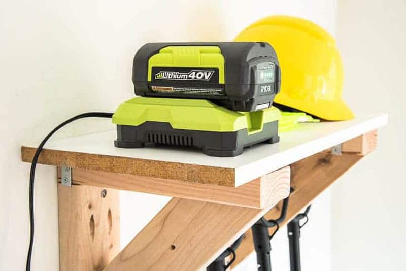 battery charger and hard hat sitting on shelf of garden tool storage rack