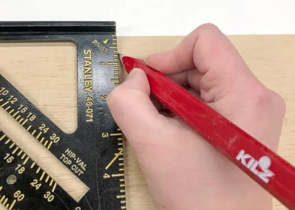 hand drawing a line on a piece of plywood with a speed square