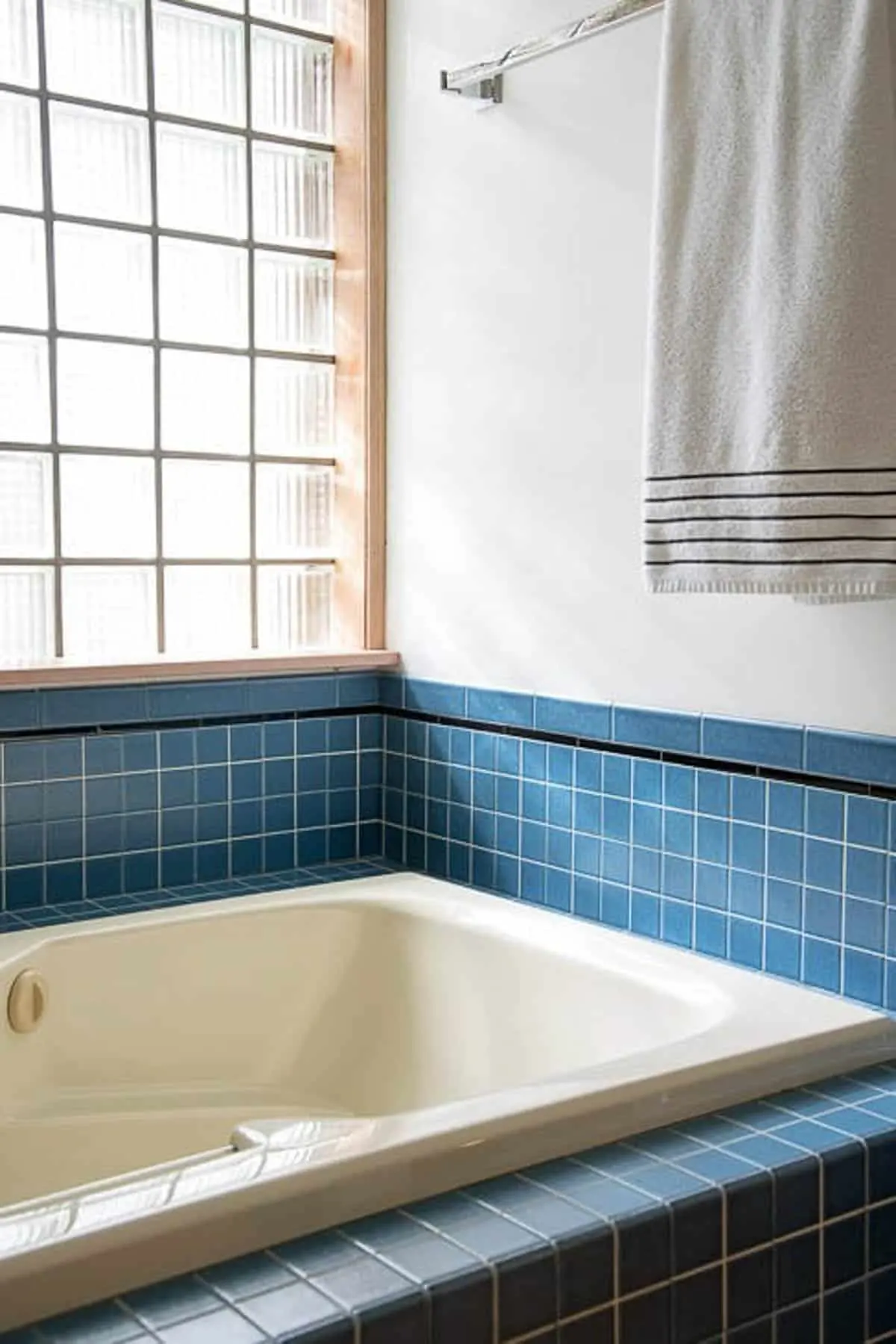 Almond bathtub with blue tile walls and glass block window