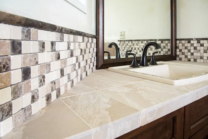 bathroom vanity with mosaic stone tile backsplash and limestone countertop