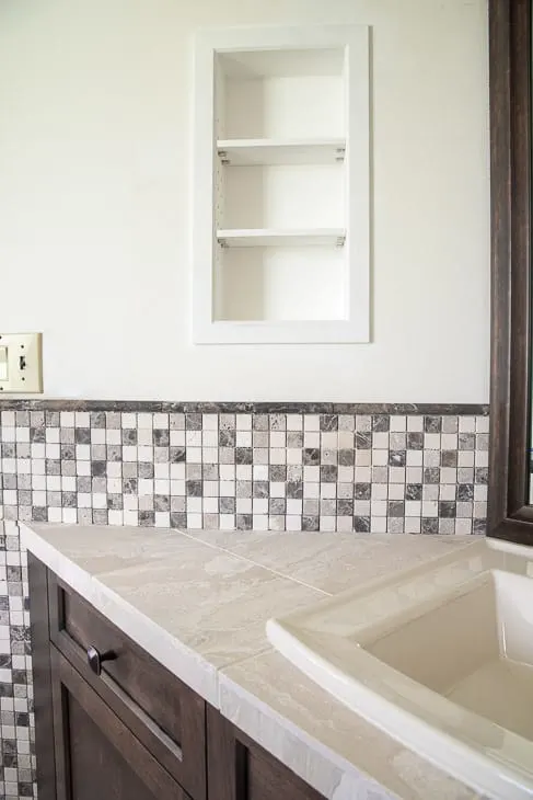 bathroom vanity with stone mosaic tile backsplash and recessed shelves above