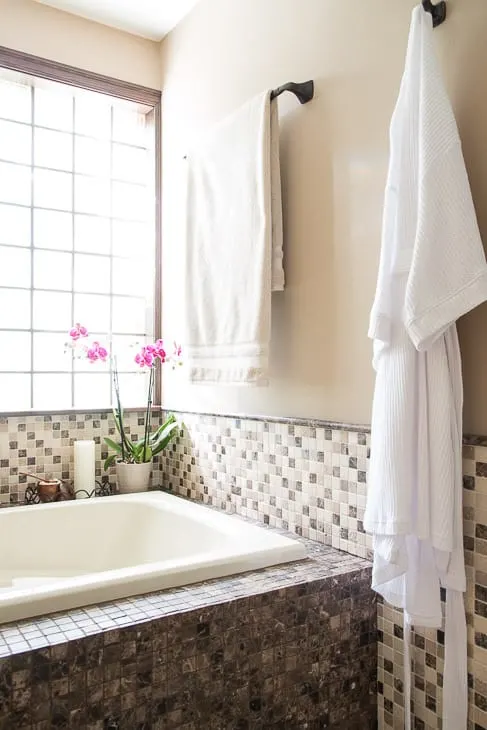 bathtub with mosaic tile walls, towel and robe hanging on wall
