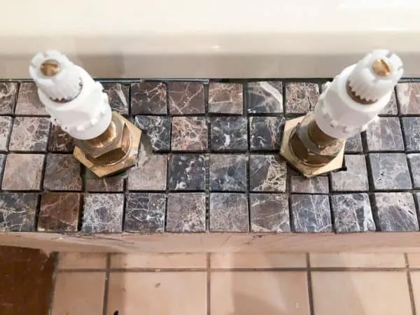 bathtub surround with deck mounted faucet handles and cut mosaic tiles