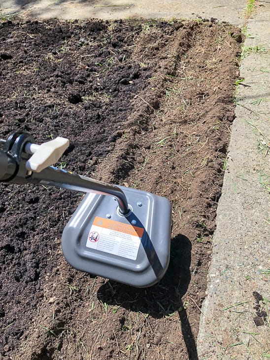 Ryobi cultivator tilling soil in overgrown garden