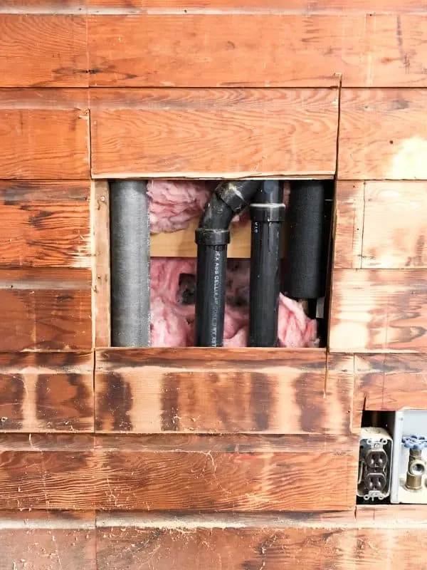 plank wall with hole cut out to access pipes