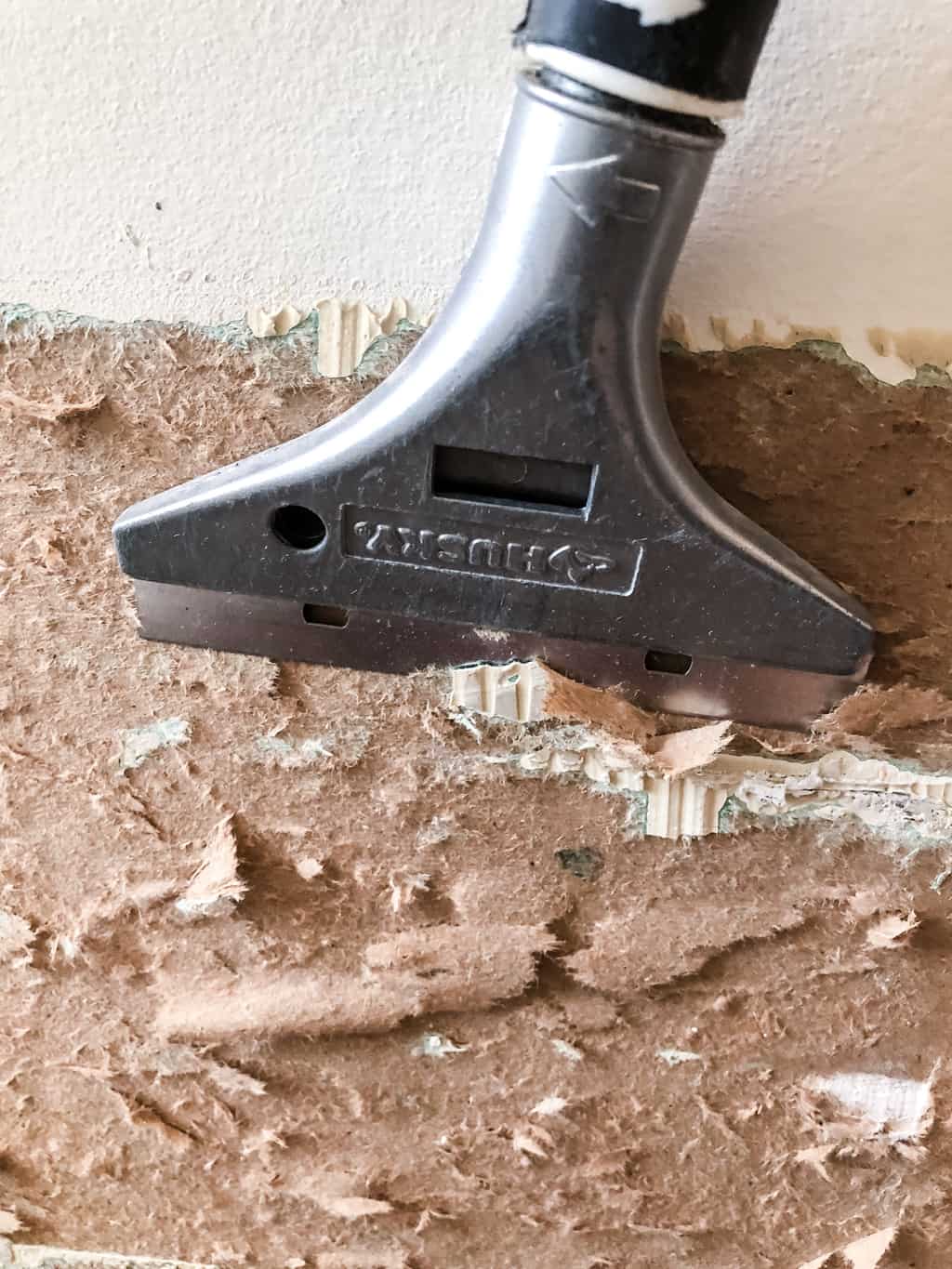scraping away loose, torn drywall paper with a scraper tool