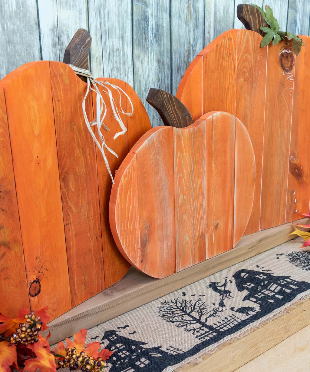 three wooden pumpkins made from pallets on a burlap table runner with faux leaves