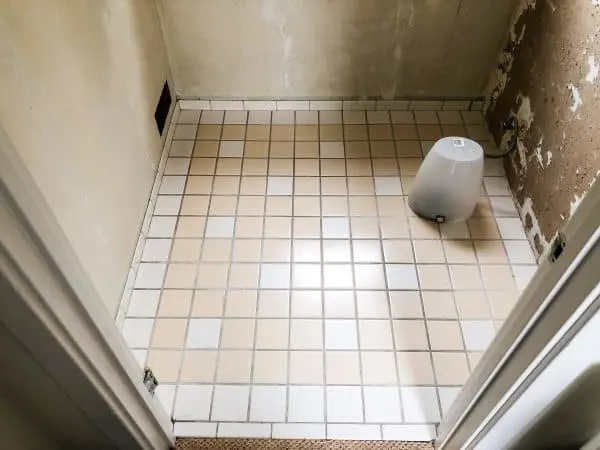 bathroom floor with toilet removed and trash can over the hole