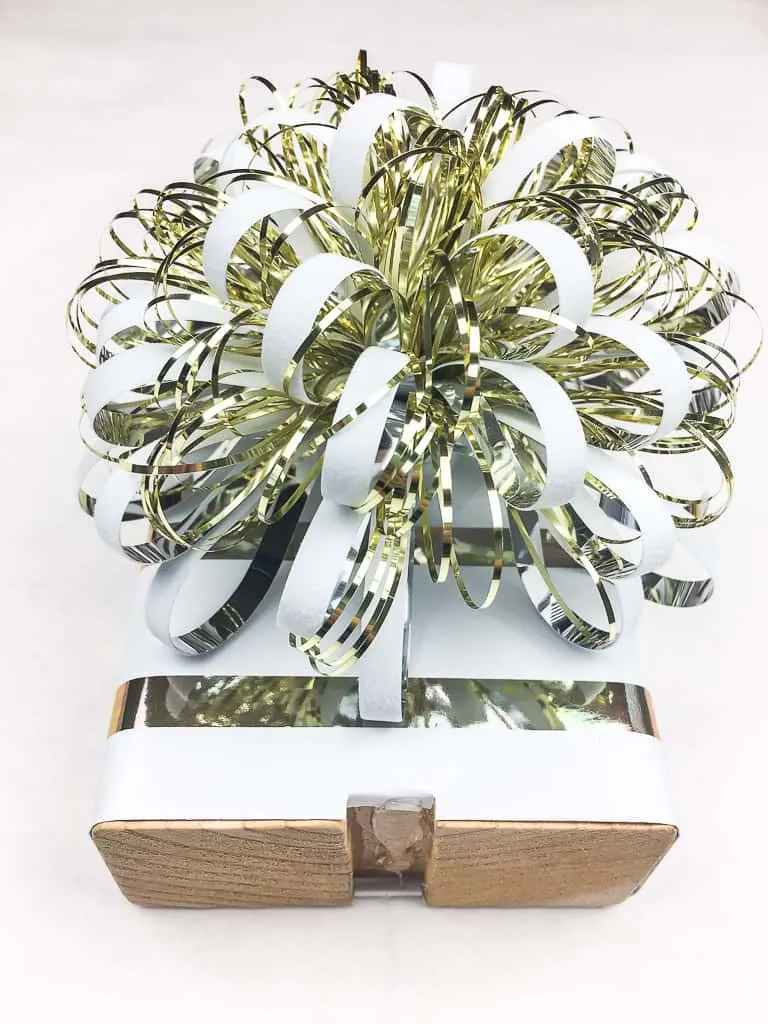 wood block covered in wrapping paper and topped with white and gold bow