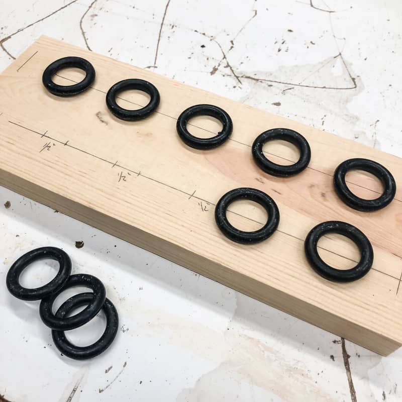 black O rings spaced apart on wood board for DIY spice rack