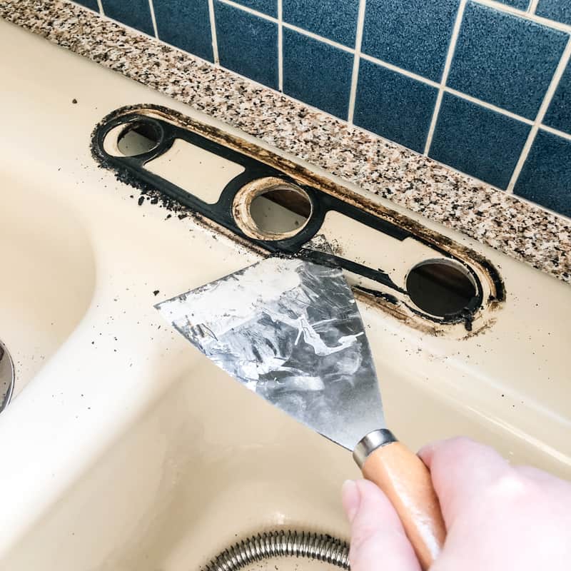 scraping black foam seal from old kitchen faucet off sink with a putty knife