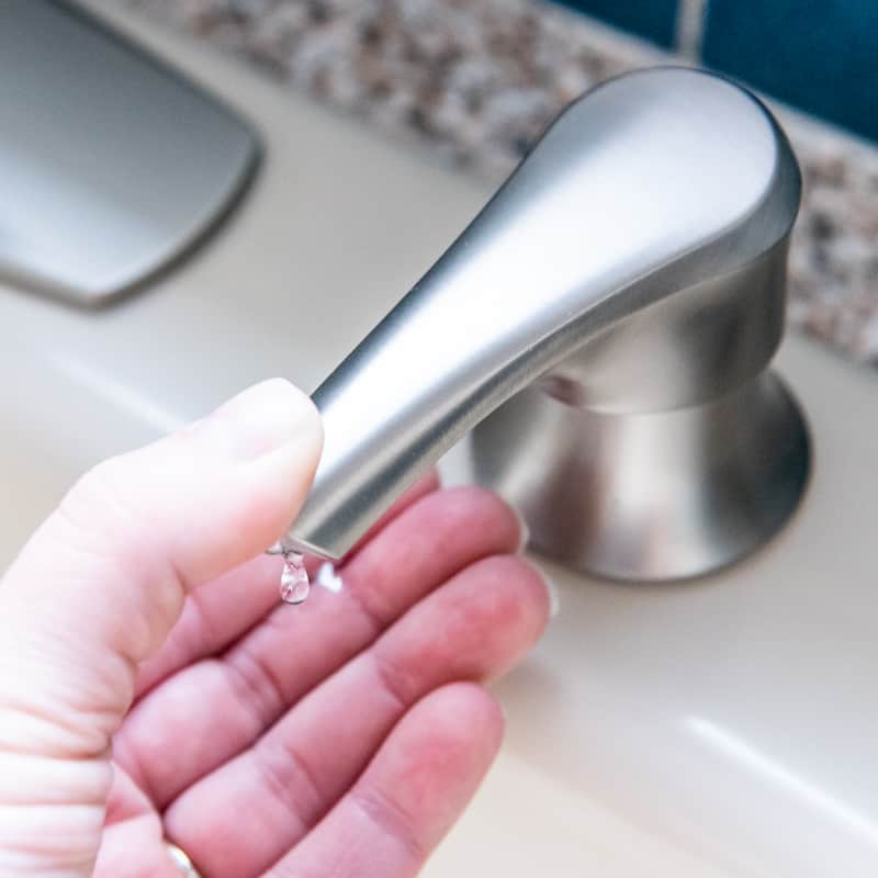 kitchen sink soap dispenser with thumb pressing on end and soap coming out
