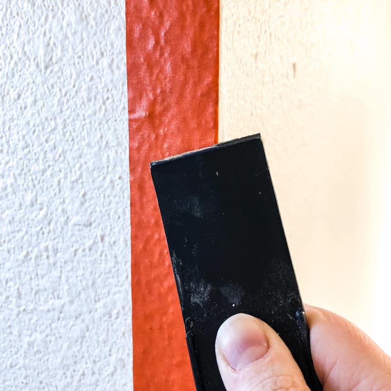 rubbing edge of painter's tape with putty knife on textured walls