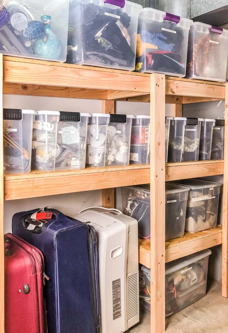 DIY garage shelves filled with plastic bins and suitcase storage underneath