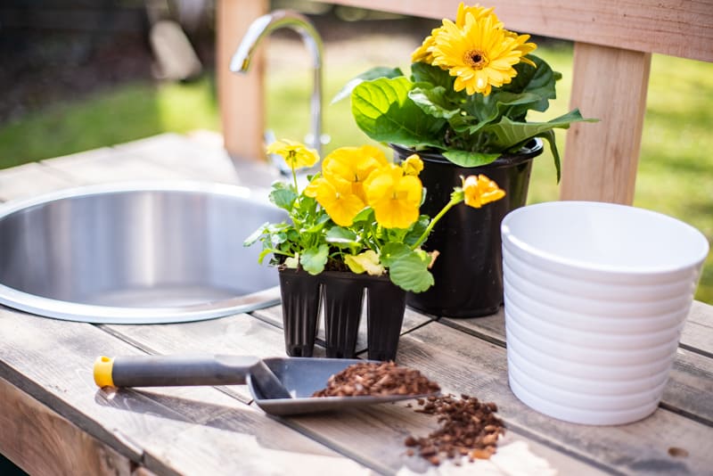 close up view of flowers and gardening tools on DIY potting bench with sink in the background