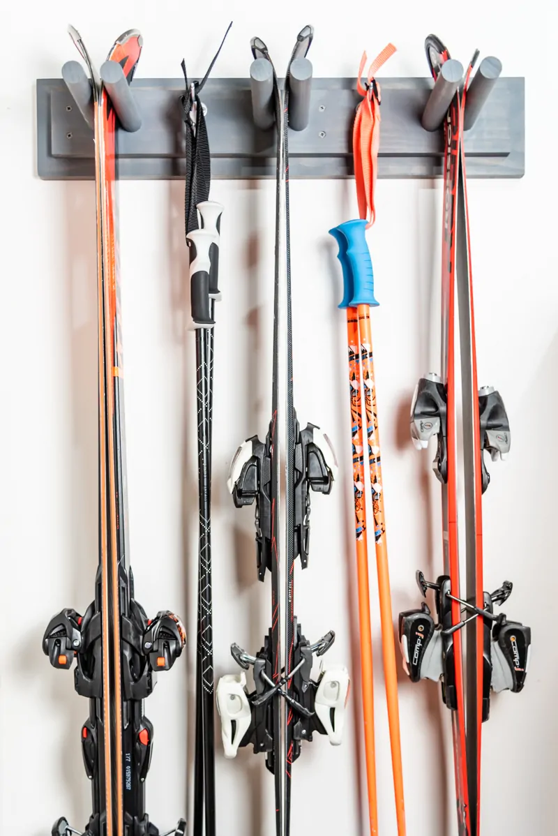 DIY ski rack with three sets of skis and two sets of poles on garage wall