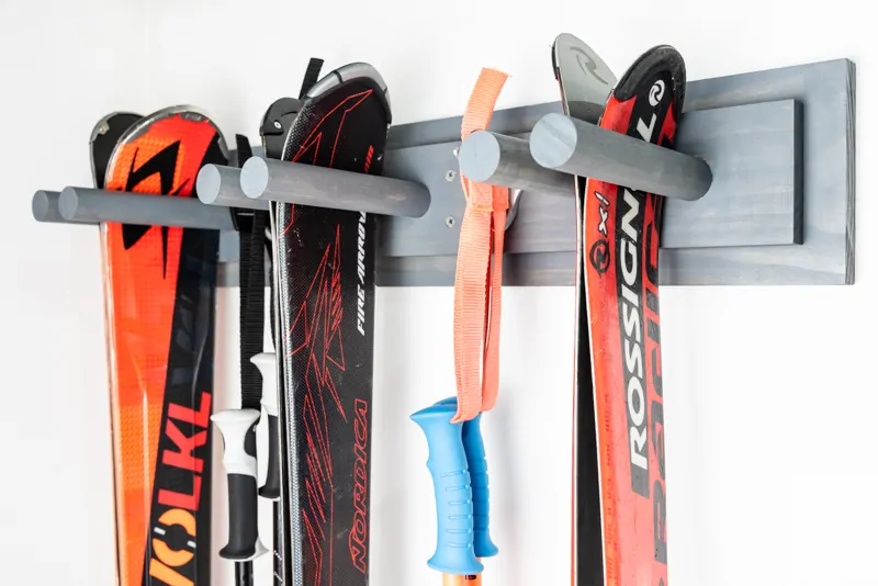 side view of DIY ski rack with three sets of skis and two sets of poles hanging on a garage wall