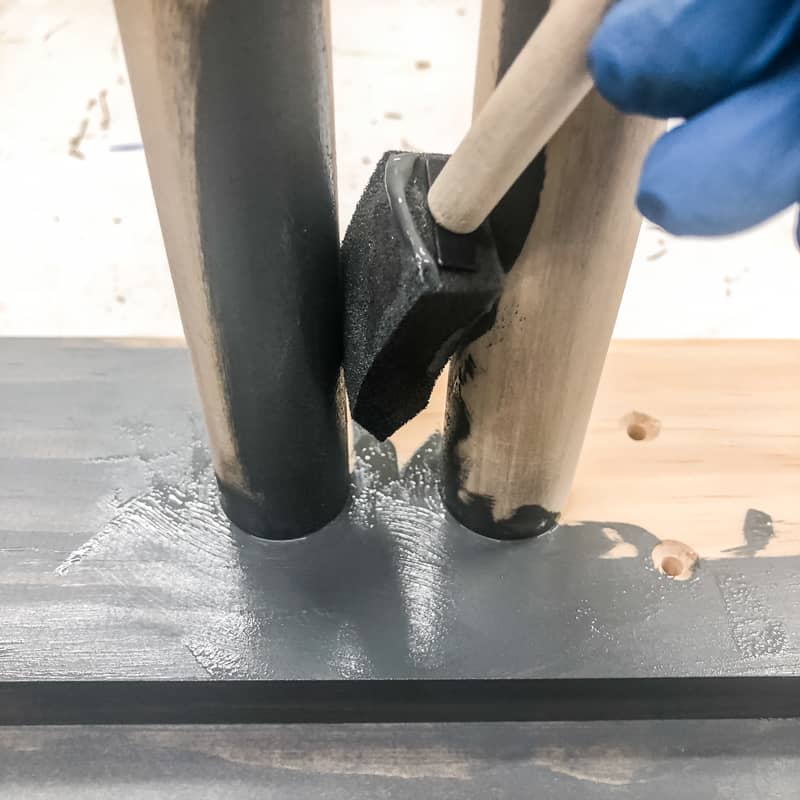applying grey wood stain to DIY ski rack with a foam brush