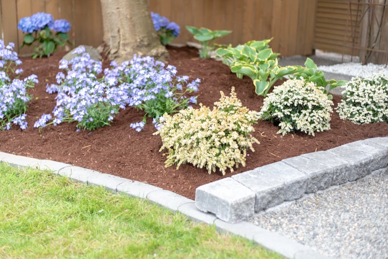 mulched garden bed next to a pea gravel patio with a block retaining wall in between