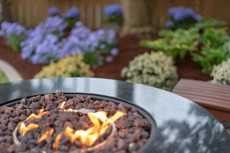 propane fire pit with flower garden in background