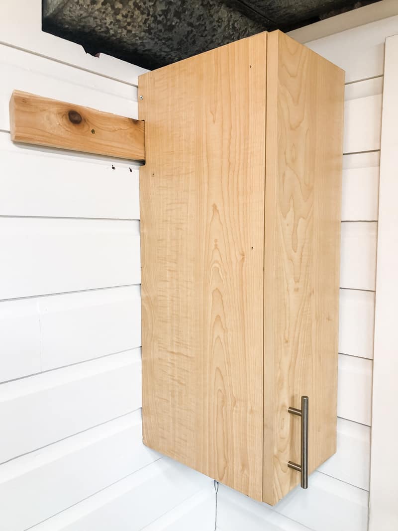 cabinet hanging from french cleat on painted wood paneling wall