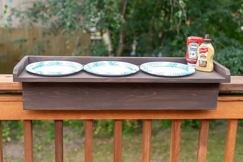 deck railing table with three paper plates and condiments