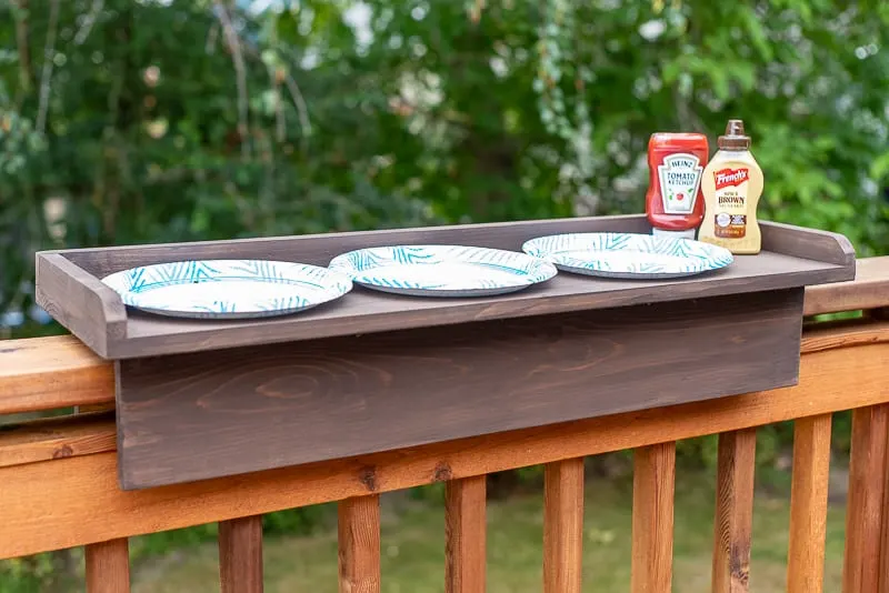 DIY balcony railing table with three plates, ketchup and mustard next to the grill