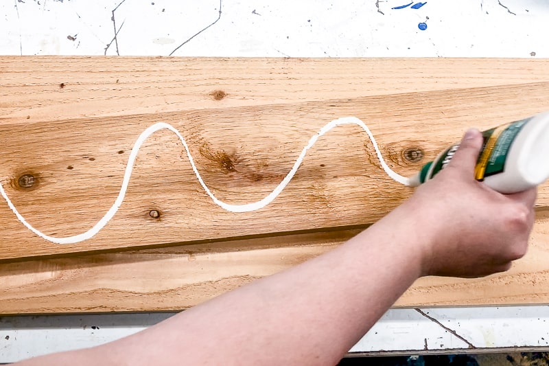 applying exterior wood glue to underside of center board of balcony railing table before screwing it into place