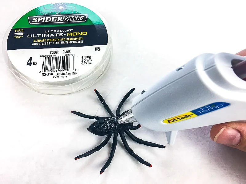 adding fishing line to back of plastic spiders with hot glue gun