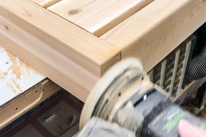 sanding the corner of the DIY outdoor coffee table frame to round over edge