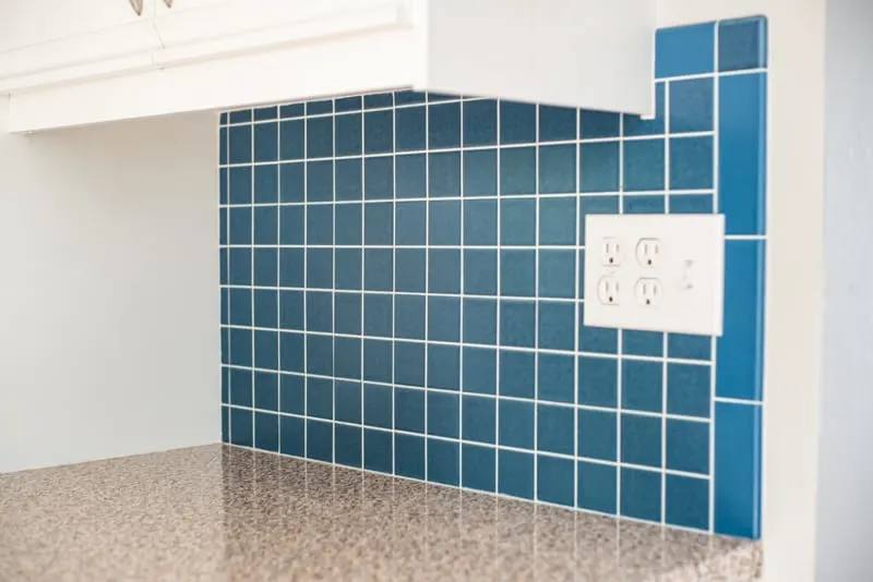 blue tile backsplash in kitchen with white cabinets and brown granite countertops