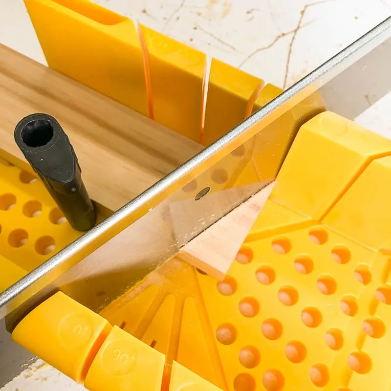 cutting bottom of DIY blanket ladder at an angle with a miter box