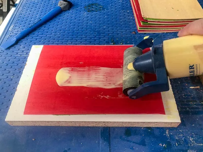 applying wood glue with a roller onto red dyed veneer