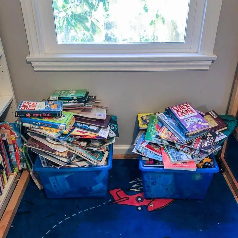blue rolling plastic bins overflowing with books under window in kids room
