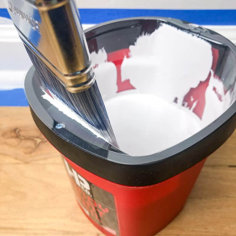 removing excess paint from a paint brush with the edge of the paint pail