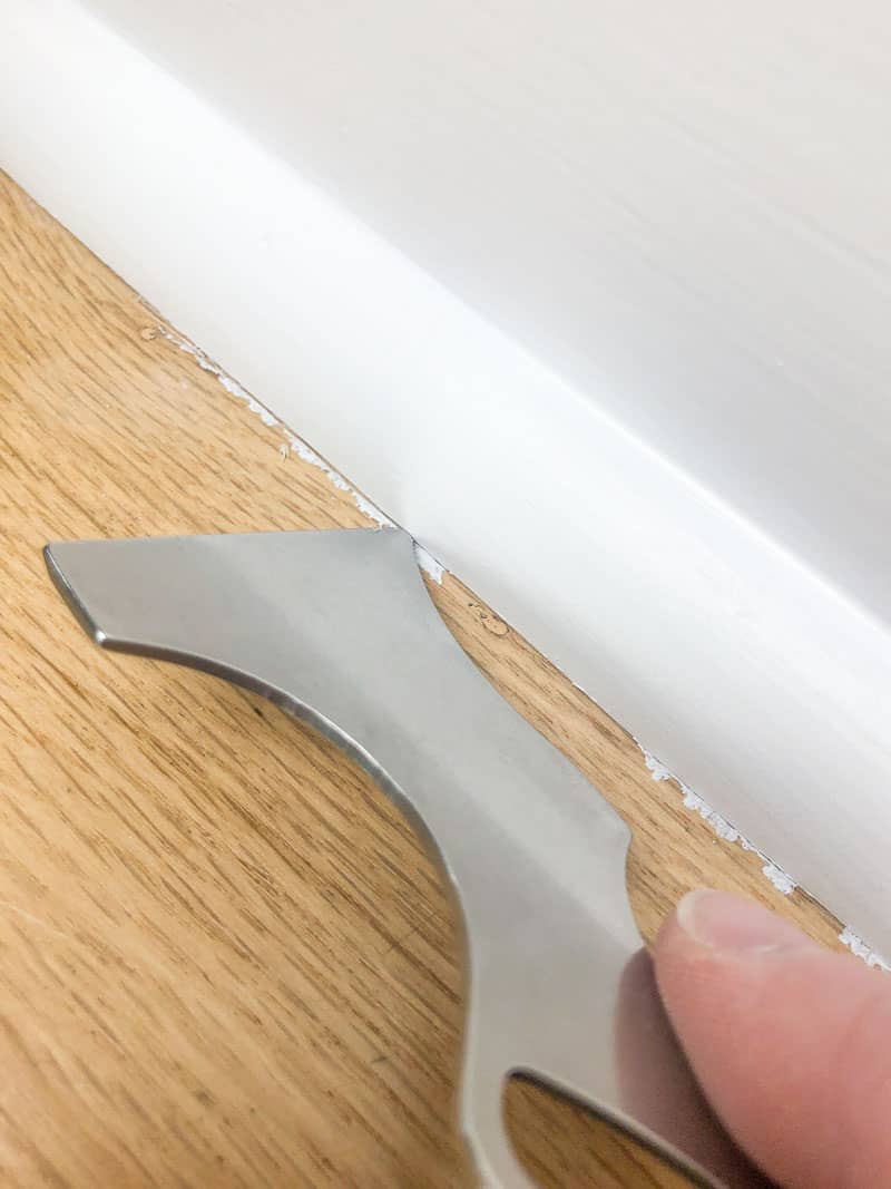 scoring seam between baseboards and floor with painter's tool